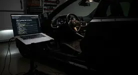 A modern black BMW is parked in a dark, clean garage, illuminated primarily by the bright screen of a laptop connected to its OBD port. The laptop screen displays a third-party automotive forum, specifically a thread about DIY coding, showing lines of code and diagnostic parameters. The scene creates a focused, high-tech atmosphere of a car enthusiast working on their vehicle at night.